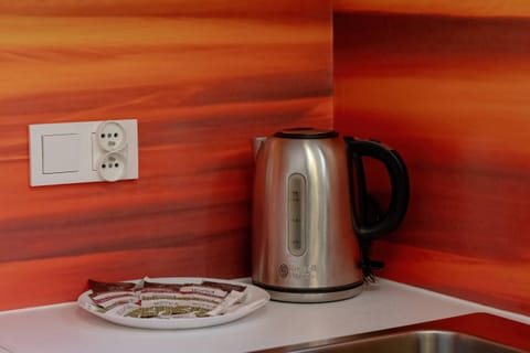 A kitchen corner with a stainless-steel kettle, a white tray, and an orange backsplash, blending convenience with modern design.







