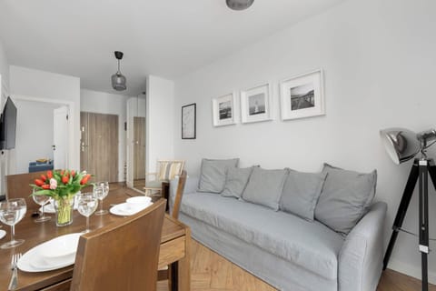 A cozy living room space with a gray sofa, a wooden dining table, and soft lighting. Perfect for relaxing or sharing meals with family and friends.