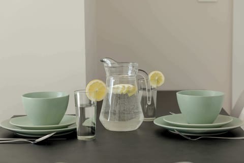 A stylish table setting with green cups, a glass jug, and a modern aesthetic. The decor is simple yet elegant.