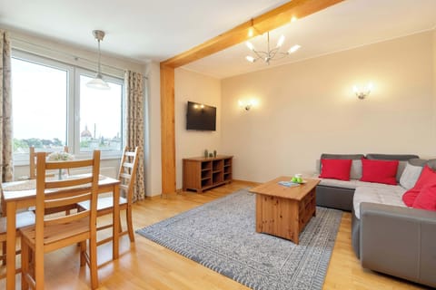A bright and spacious living room featuring a comfortable sofa, a wooden dining table with chairs, and large windows that bring in plenty of natural light.