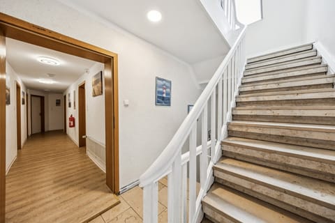 Heller Hausflur mit gepflegtem Treppenhaus, weißem Geländer und dekorierten Wänden – einladender Zugang zu den Ferienwohnungen.