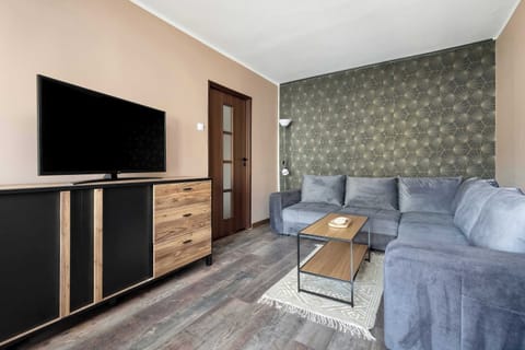 A modern living room with a flat-screen TV, wooden furniture, and a blue sofa arranged on a neutral rug.