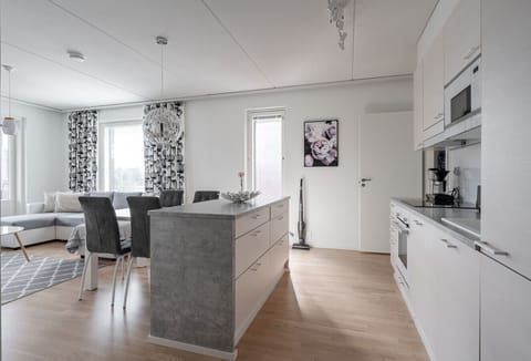 A bright, modern open-plan kitchen and living area featuring stylish grey accents, a cozy dining space, and large windows that fill the room with natural light.