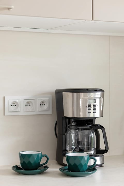 A close-up of a coffee machine setup with matching green cups and a modern backsplash.