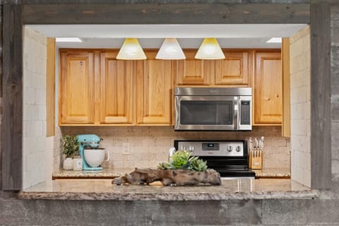 Bright, fully stocked kitchen with generous counters and a window overlooking the cozy living room—stay connected while you cook.