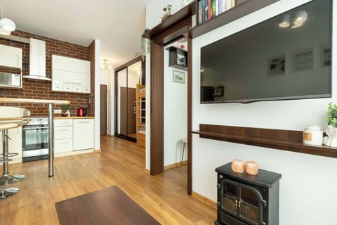 A galley-style kitchen with white cabinets, brick backsplash, and a slim corridor leading toward the entrance.