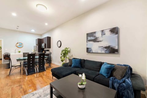 A welcoming open-concept living and dining area featuring a plush sectional, modern artwork, and a spacious dining table. Perfect for relaxing, enjoying meals together, and gathering in a bright, comfortable setting.