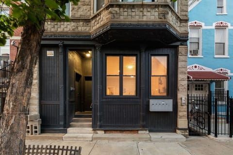 A brick building exterior with a black entrance, large windows, and a small front step leading to the doorway.
