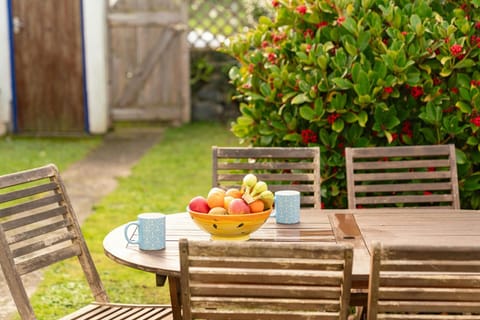 Patio table and chairs with a bowl of fruit. Small lawn and path to rear gate