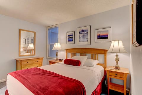 This cozy studio features a queen bed adorned with plush pillows and bedside tables, offering a serene atmosphere enhanced by tasteful artwork.