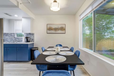 A bright dining space with modern blue chairs and a sleek table, perfect for family meals or game nights, with large windows framing views of the backyard and pergola.