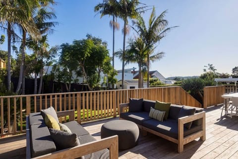 Sunny deck leading off the living space, with outdoor lounge seating and dining, and steps down to the lawn