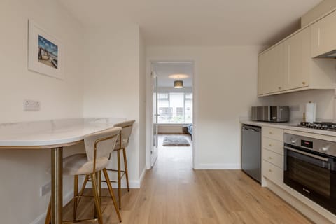 View from modern kitchen featuring cream cabinets and marble breakfast bar into bright living room with large window.