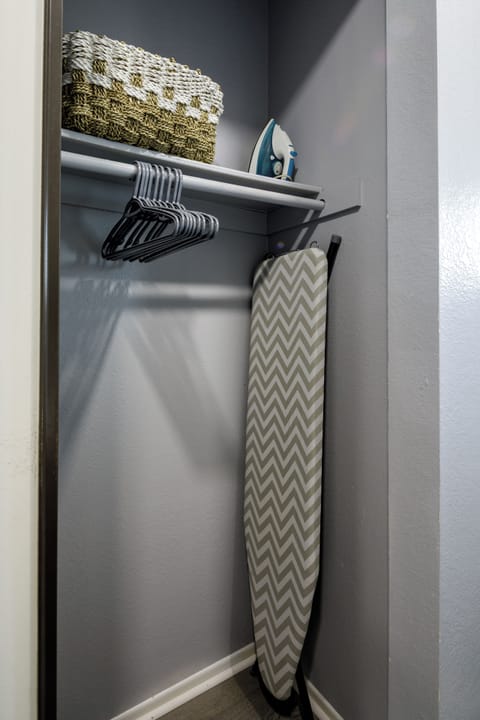 A well-stocked guest closet with hangers, an iron and ironing board, and fresh towels neatly arranged on the top shelf — everything you need for an extended stay.