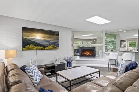 Bright living room w/ large sectional, wall-mounted TV & big windows bringing in natural light