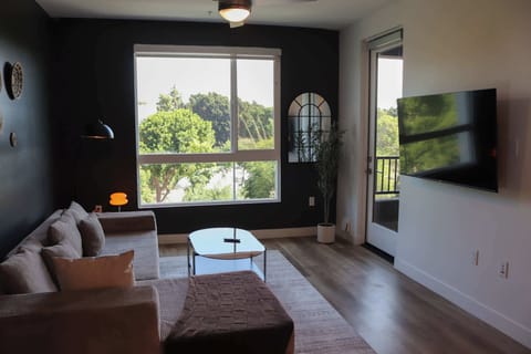 Spacious living room featuring a cozy L-shaped sofa, a full-size air mattress, and a 65" Smart TV with preloaded access to Netflix, Hulu, and Disney+, all set up for your enjoyment.