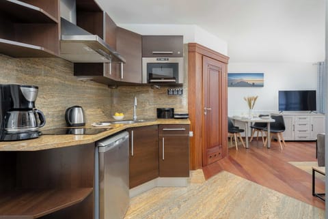 A small, tidy kitchen with white cabinets and stainless-steel appliances. Open shelves display plants and dishes, giving the space a fresh and functional feel.