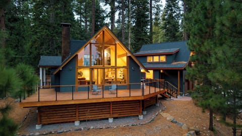 Warm, glowing cabin surrounded by towering pines with a wraparound deck made for mountain living.