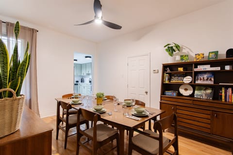 Dining room with a mid-century table set for six, complemented by modern décor, greenery, and a curated bookshelf for a warm, welcoming touch.