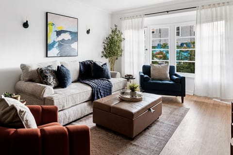 Airy living space featuring a plush sofa, expansive bay window to enjoy the Pacific breeze, and flowing white curtains.