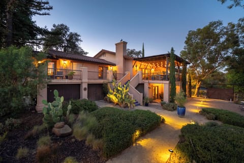Beautiful Spanish-style villa nestled among mature trees, featuring warm architectural lighting and manicured landscaping that creates an inviting arrival experience.