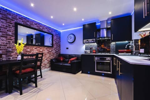 Dining, lounging, and cooking share one stylish space lit by blue LEDs, with an exposed brick feature wall tying the whole room together.