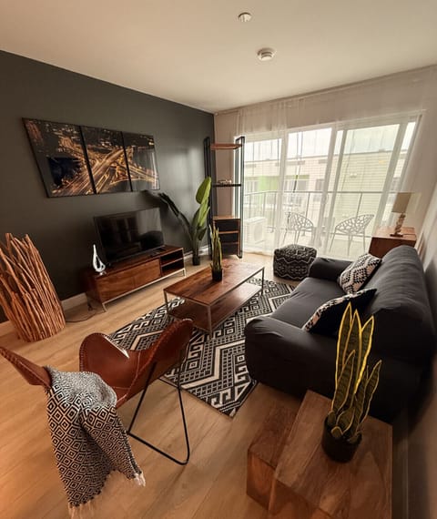 Unwind in a stylishly curated main living room featuring a plush dark sofa, cognac leather butterfly chair, two-tier coffee table, flat-screen TV on a wooden console, and large sliding glass doors leading directly to your private balcony.