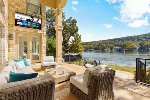 Covered stone terrace and wicker seating overlook Lake Austin