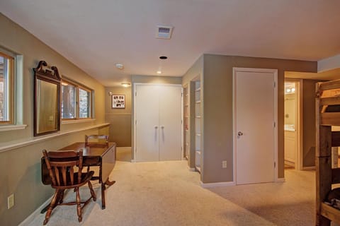 A carpeted room with a small desk and chairs, wall mirror, built-in shelving, and a view into an adjacent bathroom.