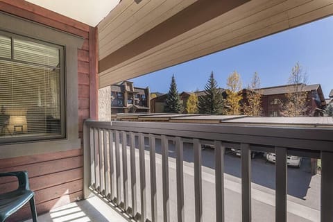 A view from a balcony with a chair. Overlooks a parking lot, apartment buildings, trees with autumn foliage, and a clear sky.