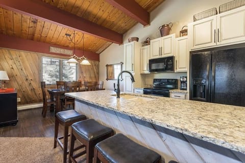 Kitchen and dining area with wooden ceiling and walls, granite countertop island with stools, modern appliances, and light fixtures; window view of outside greenery.