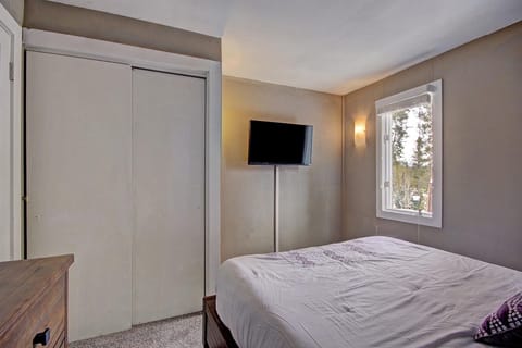 A small bedroom with a bed against the right wall, a wall-mounted TV, a window, a wooden dresser, and a closet with sliding doors.