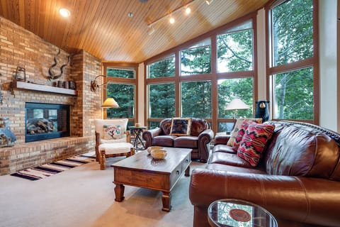 Curl up by the fireplace in this inviting living space, where soaring windows frame lush forest views and leather seating invites you to unwind in natural warmth and comfort.