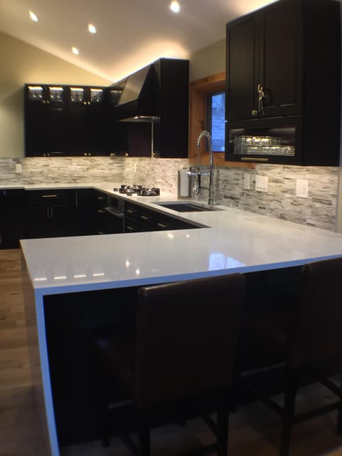 New kitchen with quartz countertops, glass backsplash, and custom lighting.