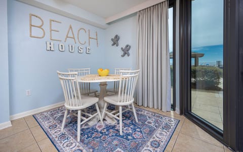 Bright blue walls complement a round dining table with white chairs, accented by a view of the beach through large windows