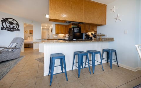 A cozy breakfast bar with blue stools complements the kitchen's wooden cabinetry, leading to a welcoming bedroom