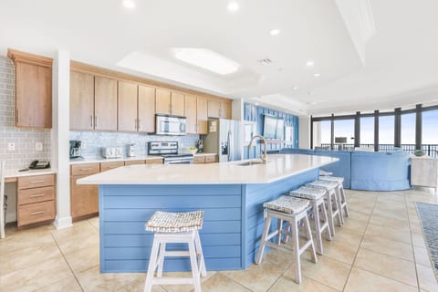 The kitchen features sleek modern appliances, a spacious blue island with seating, and a costal vibe to compliment your stay