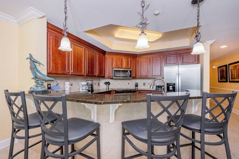 Modern kitchen with dark granite countertops, stainless appliances, and stylish bar seating with elegant lighting