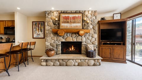 Gather around the glowing stone fireplace in this inviting living space with mountain-inspired décor, a flat-screen in the entertainment center, and a balcony just steps away.
