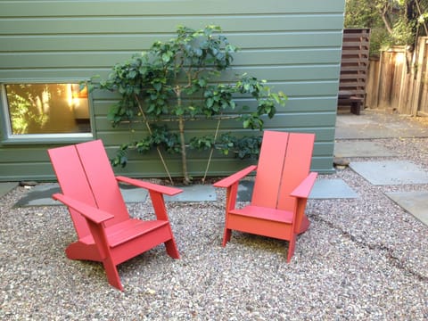 A sitting area is next to the front door; yard features mature trees, succulents