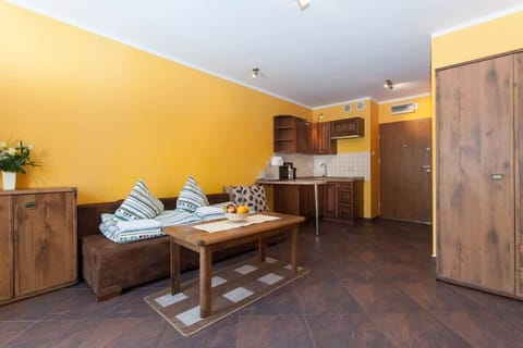 A dining area with a wooden table and cushioned chairs, situated next to the kitchen. The yellow walls and wood floors create a warm and cozy atmosphere.