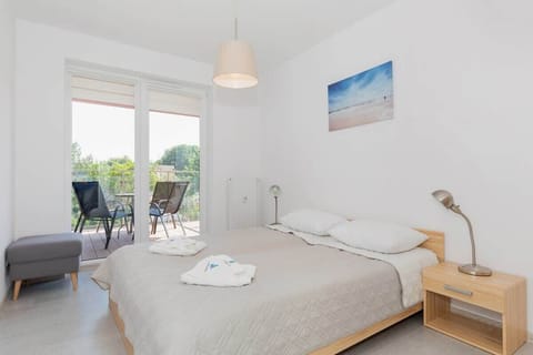 Bright bedroom with double bed with grey bedspread. Plenty of natural light streams in through the large windows.