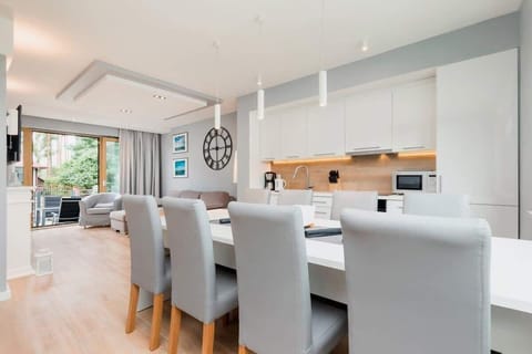 A modern kitchen and dining area with a white, minimalist design, featuring a spacious dining table for six and a sleek kitchen setup with wooden accents.
