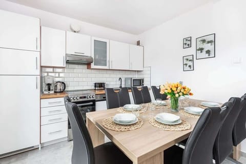 A modern kitchen and dining area with a wooden table set for four. The kitchen has white cabinets and stainless steel appliances, providing a functional and aesthetically pleasing space.