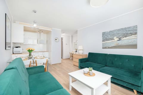 A compact space with a green sofa, a dining table, and a small kitchen area in the background.