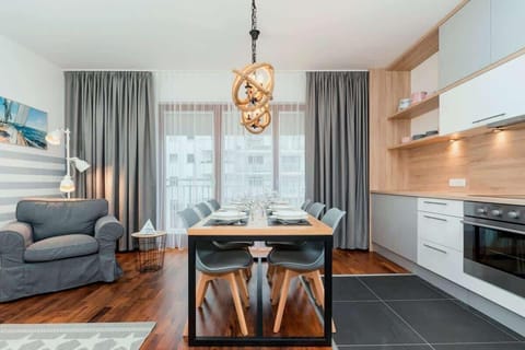 The living room from a different perspective showing a large table for 6 people. A disagner lamp hangs above the table. To the right is the kitchenette matching the design of the entire room.