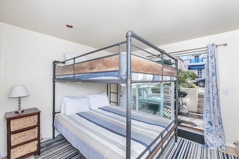 Lower level bedroom provides Queen over Queen bunk bed, linens, TV, closet, sliding glass door out to front sub-street patio and seating.