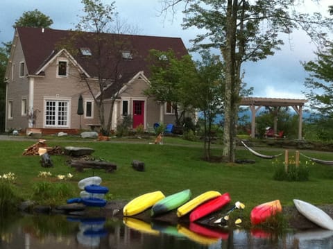 Summer view of the main house from the pond-- pergola, firepit, kayaks & hammock