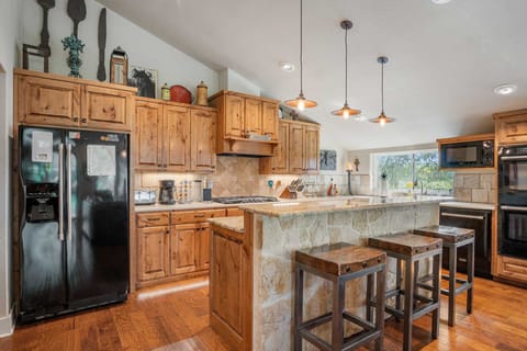 A rustic kitchen features knotty pine cabinets, a stone-clad island with bar stools, modern appliances, and decorative accents.