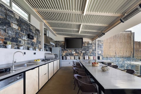 A Fully equipped outdoor kitchen under the pergola with TV, hobs, dishwasher, toaster and coffee machine